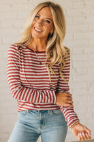 Woman wearing a red and white striped long-sleeve shirt and light blue jeans against a white brick wall.