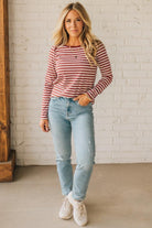 Woman wearing a red and white striped shirt and light blue jeans against a white brick wall.
