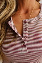 Close-up of a woman wearing a red and white striped henley top with a gold necklace.