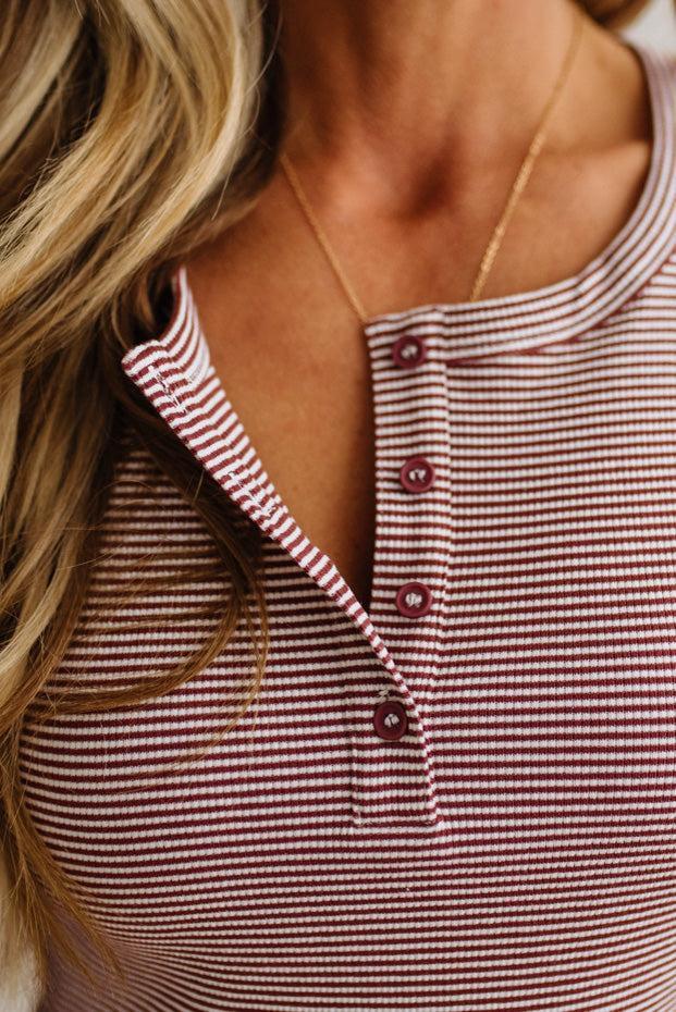 Close-up of a woman wearing a red and white striped henley top with a gold necklace.