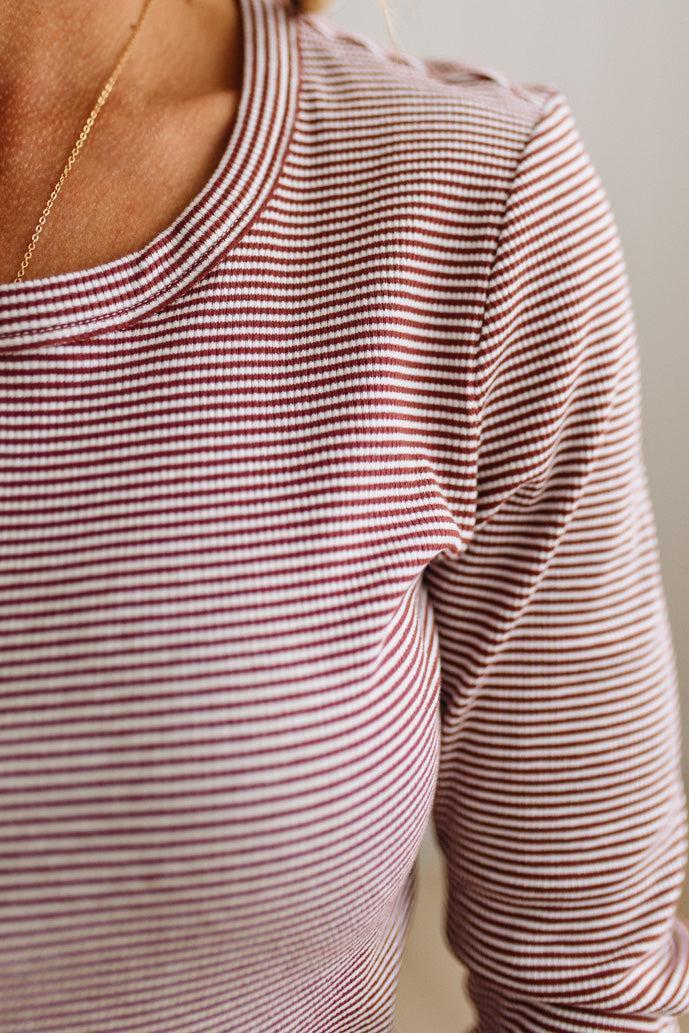 Close-up of a person wearing a long-sleeve crewneck top with fine horizontal red and white stripes, paired with a delicate gold chain necklace.