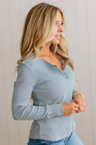 A woman wearing a long-sleeve V-neck top with thin horizontal blue and white stripes, paired with blue jeans, standing against a light beige paneled wall.