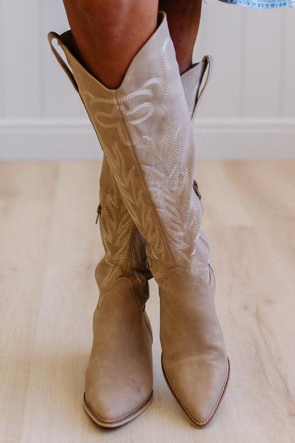 Beige cowboy boots on a light wooden floor