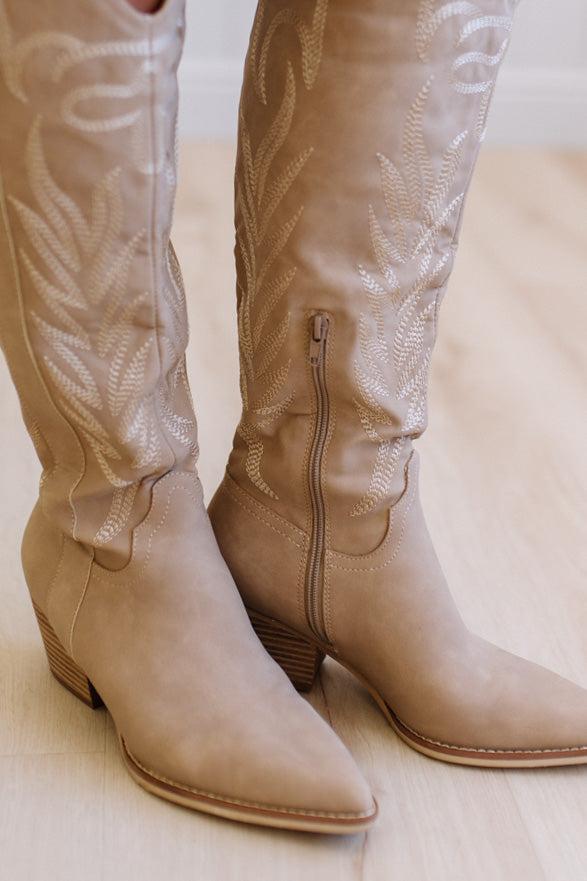 Pair of beige knee-high boots with detailed patterns on a light background