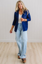 Woman wearing a blue blazer, white top, and light blue jeans indoors.