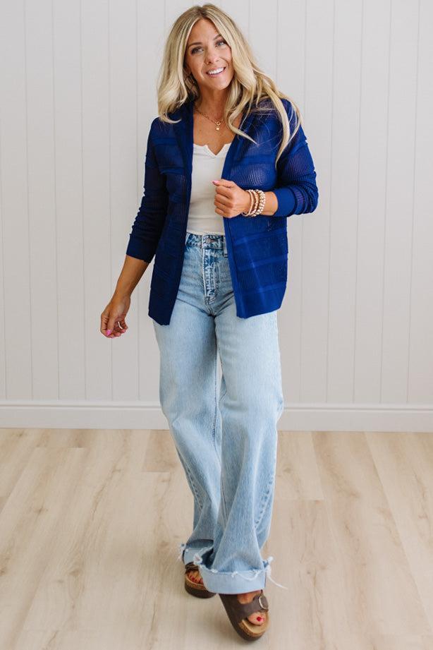 Woman wearing a blue blazer, white top, and light blue jeans indoors.