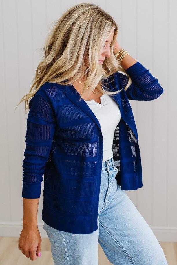 Woman wearing a blue cardigan over a white top and light blue jeans.