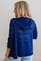 Woman wearing a blue textured jacket with a hood against a white wall.