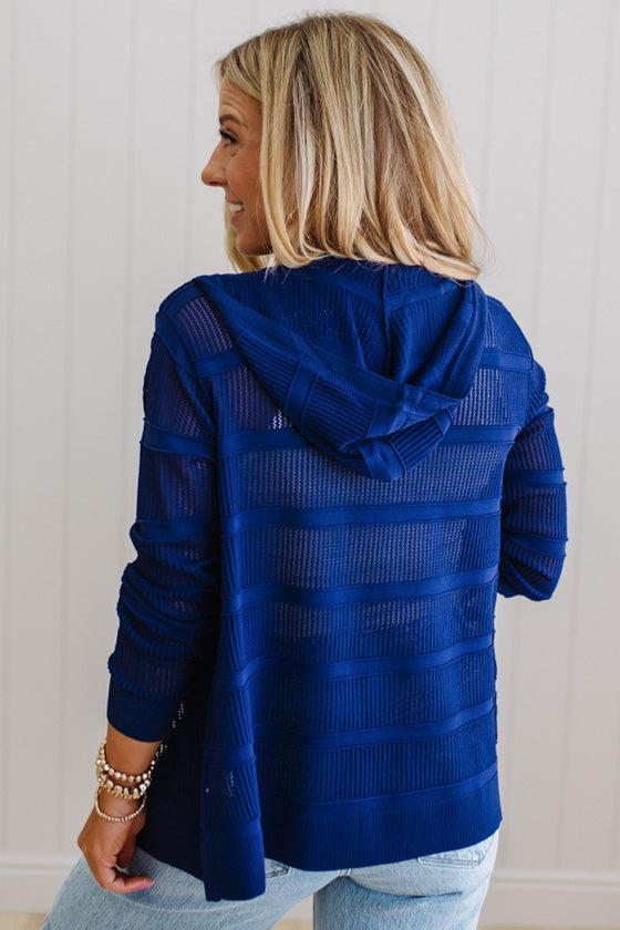Woman wearing a blue textured jacket with a hood against a white wall.