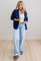 Woman wearing a blue blazer, white top, and light blue jeans against a white wall.