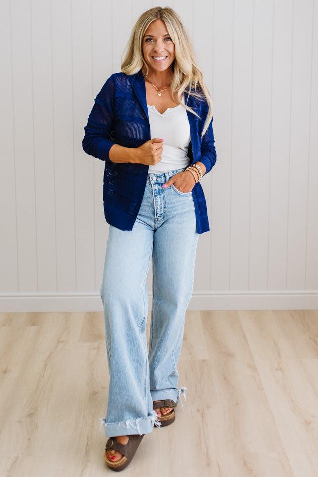Woman wearing a blue blazer, white top, and light blue jeans against a white wall.