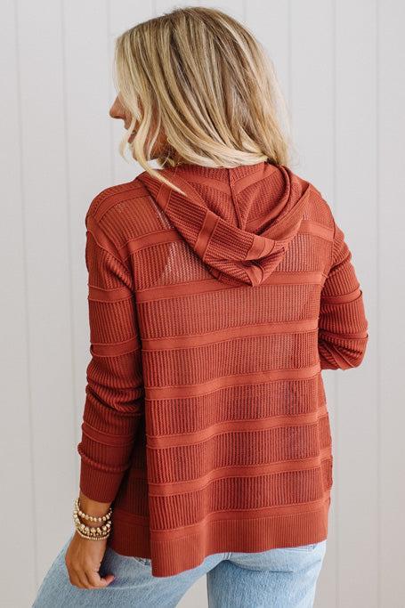 Person wearing a rust-colored ribbed hoodie against a white background