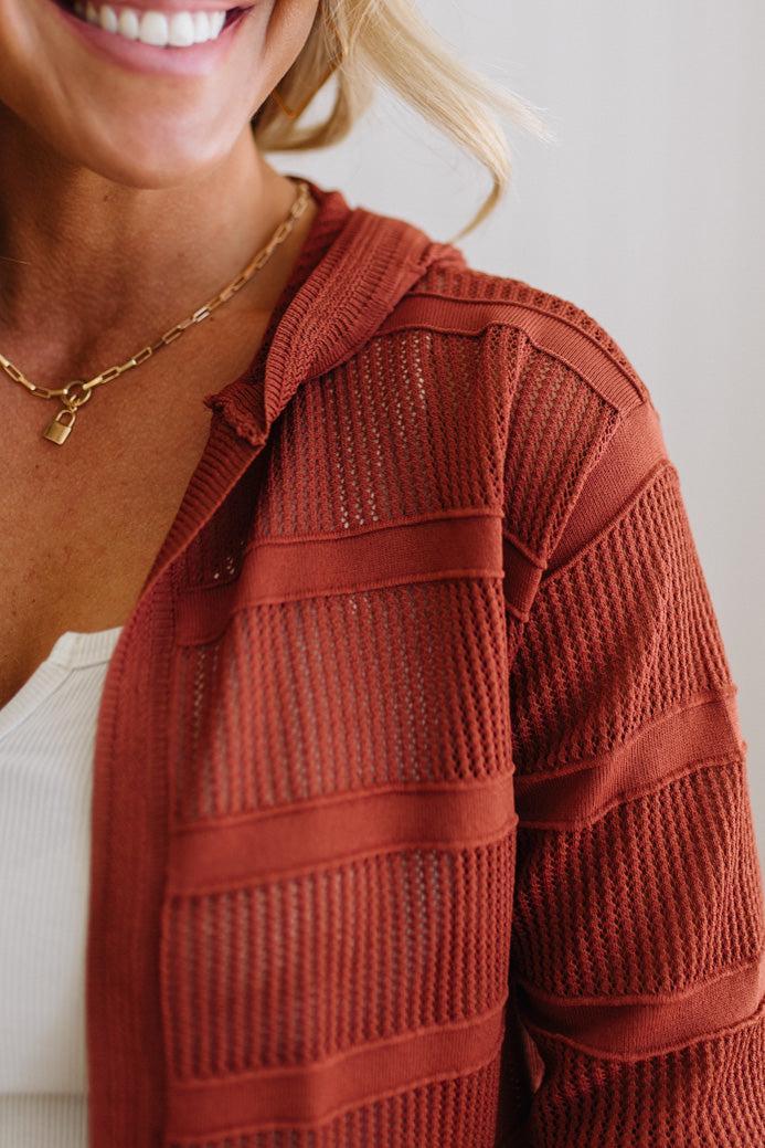 Close-up of a person wearing a rust-colored knit cardigan with a plain background