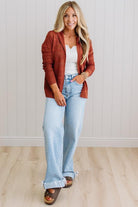 Woman wearing a rust-colored cardigan, white top, and light blue jeans against a white wall.