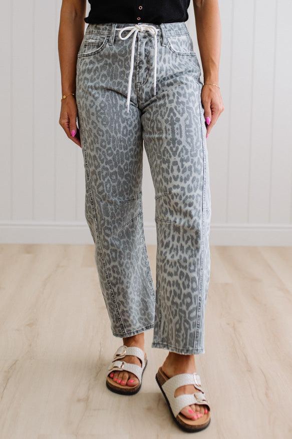 Person wearing leopard print pants and white sandals on a light wooden floor.