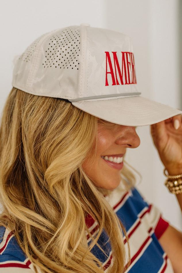 Woman wearing a beige cap with 'AMERICA' printed on it, smiling.