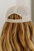 Beige baseball cap with mesh back worn by a person with long blonde hair.