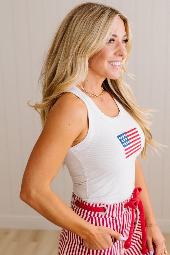 Woman wearing a white tank top with an American flag design and a red and white checkered skirt.