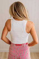 Person wearing a white sleeveless top and red striped pants with a neutral background