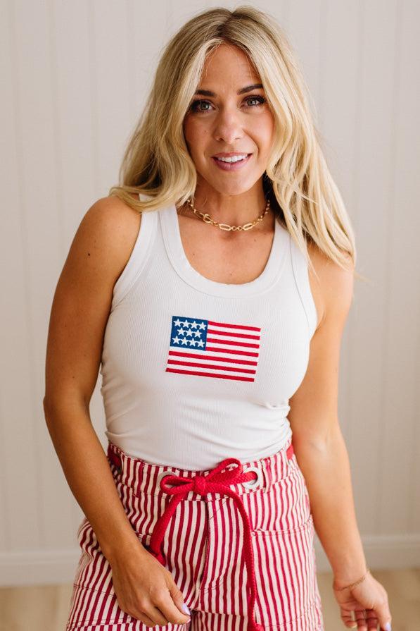 Woman wearing a white tank top with an American flag design and red striped pants.