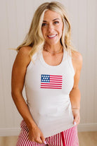 Woman wearing a white tank top with an American flag design against a plain background