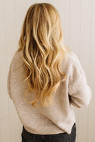Person wearing a beige sweater with long blonde hair, standing against a neutral background