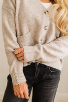 Person wearing a beige button-up sweater and black jeans against a neutral background