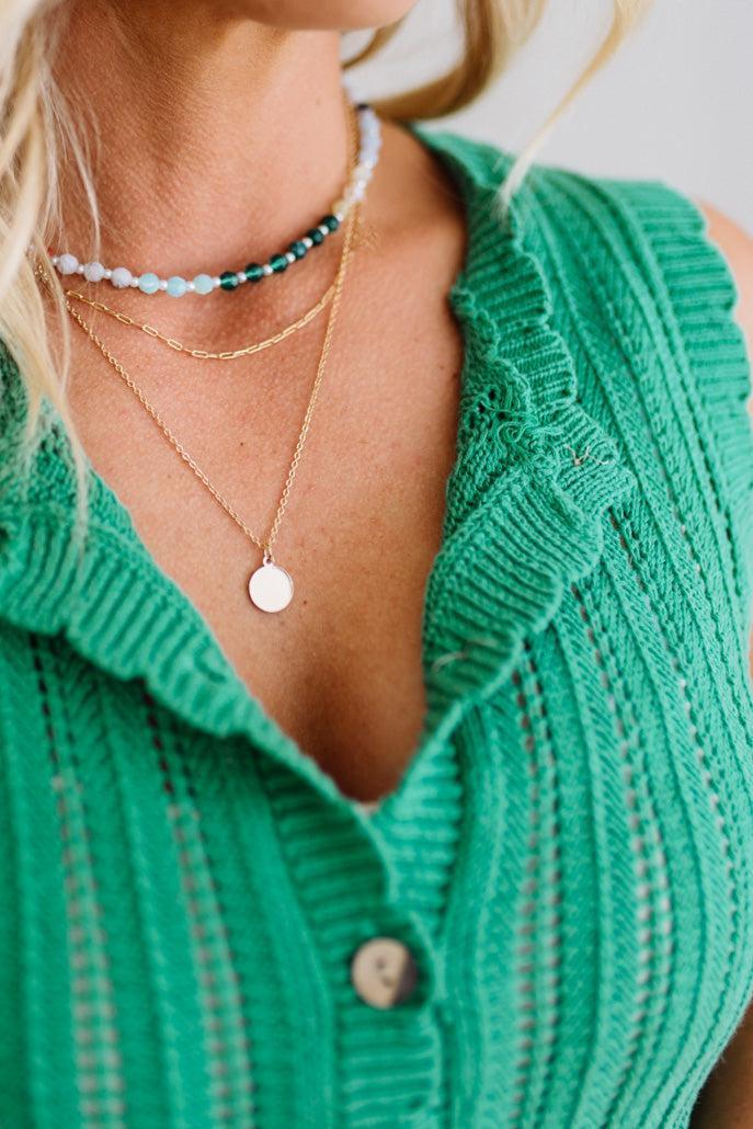 Close-up of a person wearing a green knitted cardigan and layered necklaces.