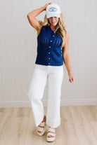 Woman wearing a blue sleeveless top, white pants, and a white cap indoors.