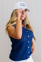 Woman wearing a blue sleeveless top and white cap with a logo against a light background