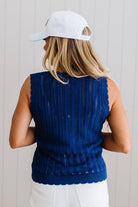 Person wearing a blue sleeveless sweater and white cap against a light background