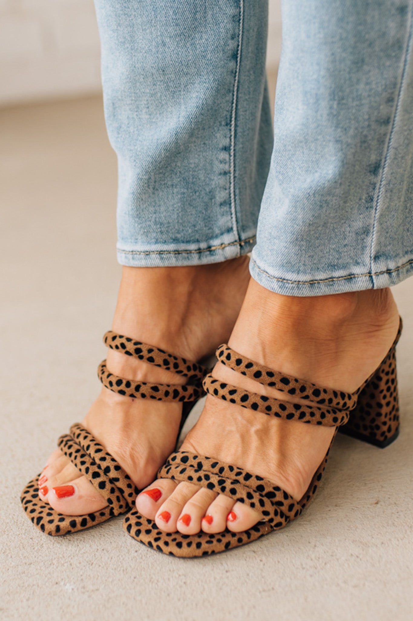 Leopard print sandals worn with light blue jeans on a neutral background