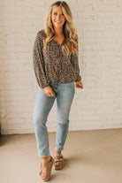 Woman wearing a leopard print top and light blue jeans against a white brick wall.