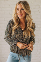 Woman wearing a leopard print top and blue jeans against a white brick wall.