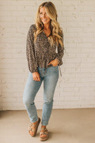 Woman wearing a leopard print top and light blue jeans against a white brick wall.