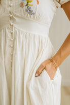 Close-up of a person wearing a white dress with floral embroidery on the chest.