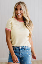 Woman wearing a yellow top with pink trim and denim shorts against a light background