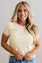 Woman wearing a yellow t-shirt with pink trim against a plain background