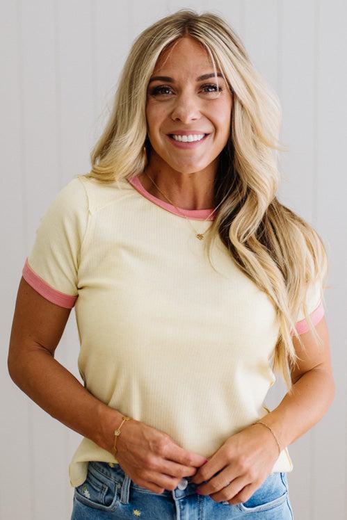 Woman wearing a yellow t-shirt with pink trim against a plain background