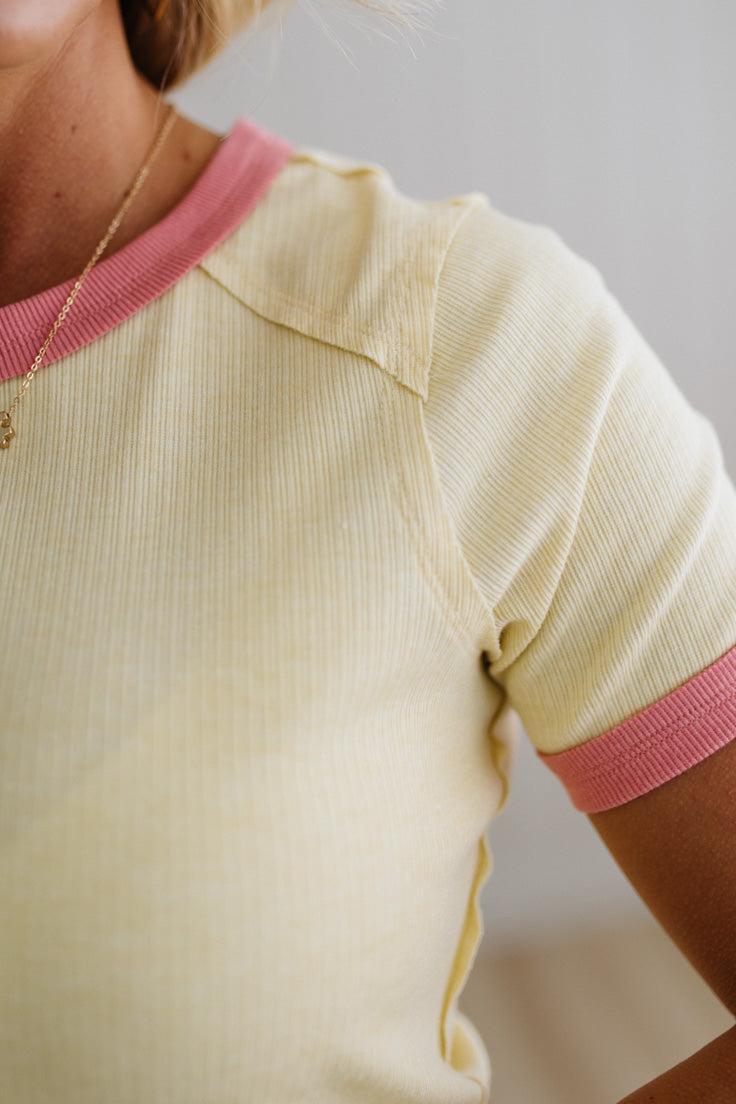 Close-up of a person wearing a yellow top with pink trim on a plain background