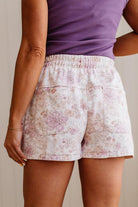 Person wearing a purple top and floral shorts against a neutral background
