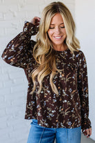 Woman wearing a brown floral blouse against a white brick wall