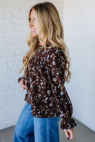 Woman wearing a floral blouse and blue jeans against a white brick wall.