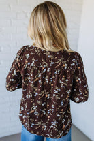 Person wearing a brown floral blouse against a white brick wall.