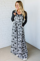 Woman wearing a black and white floral dress against a white brick wall.