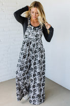Woman wearing a black and white floral dress against a white brick wall.