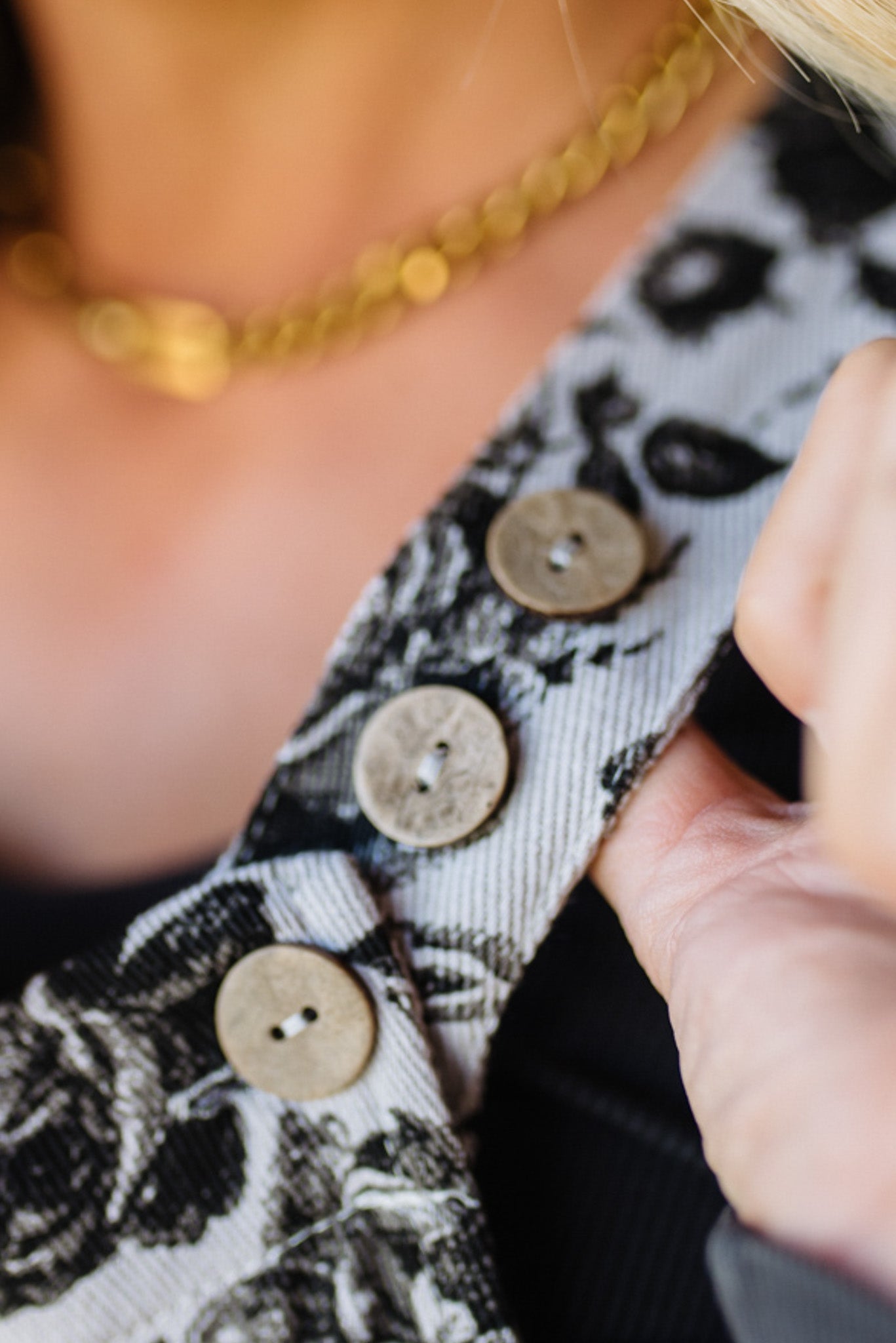 Close-up of a person wearing a patterned garment with buttons and a gold necklace.