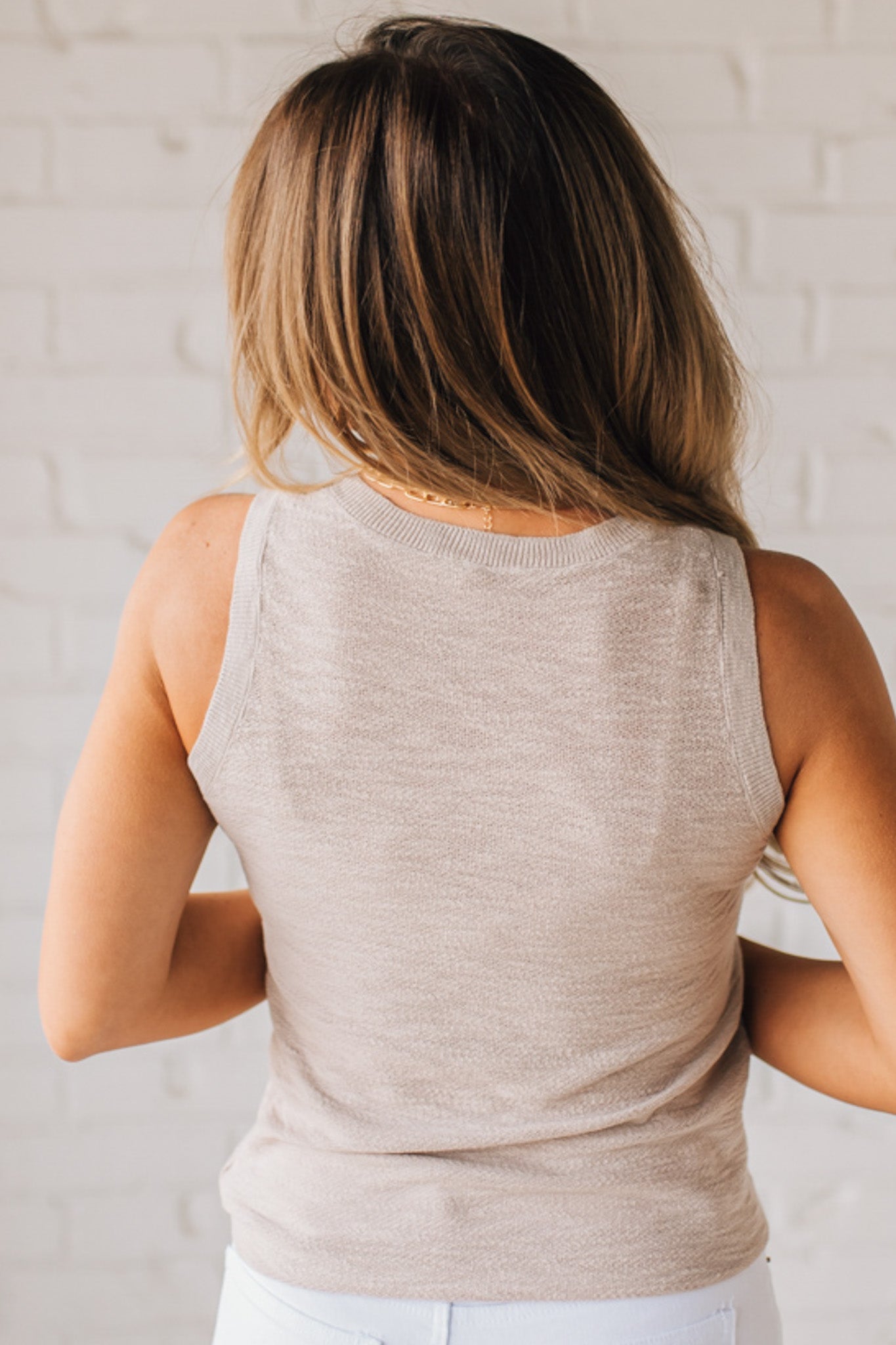 BLONDE WOMAN WEARING A ROUND NECK SLEEVELESS SLUB KNIT TOP.