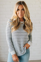 Woman wearing a striped sweater and light blue jeans against a white brick wall.