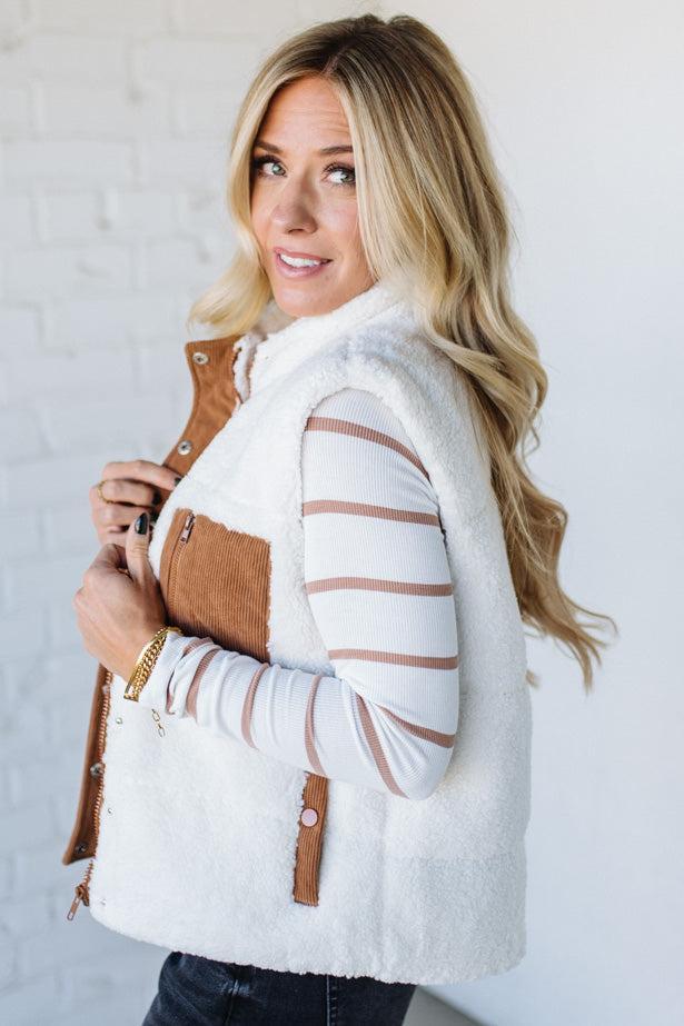 Woman wearing a white quilted vest with brown accents against a light background